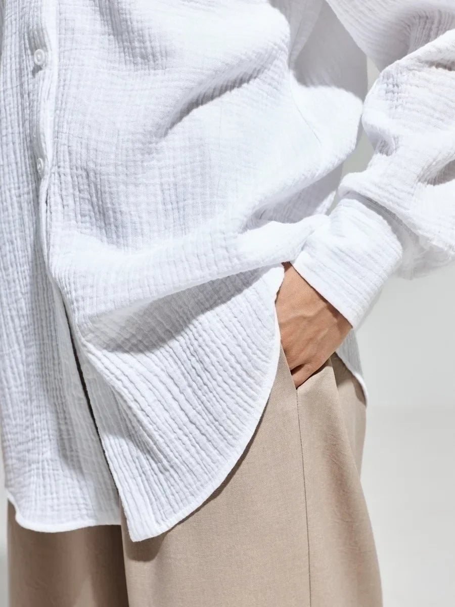 Camicia bianca in cotone a maniche lunghe, tessuto a trama leggera, abbinata a pantaloni beige. Stile casual ed elegante per uomo o donna.