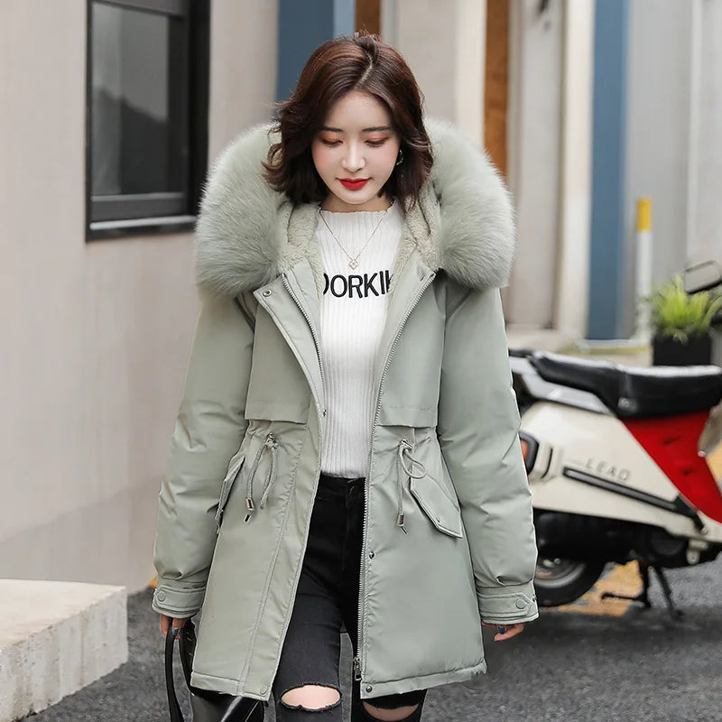 Giacca invernale donna con cappuccio in pelliccia sintetica grigia, abbinata a maglione bianco e jeans strappati. Moda casual autunno-inverno.