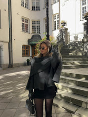 Donna alla moda con occhiali da sole, indossa cappotto grigio e gonna nera, posa in strada storica europea. Eleganza urbana, stile autunnale.