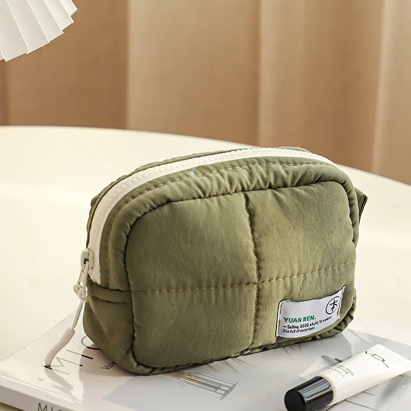Astuccio verde imbottito con cerniera, su tavolo bianco. Design moderno, ideale per cosmetici o accessori. Perfetto per viaggi e organizzazione.