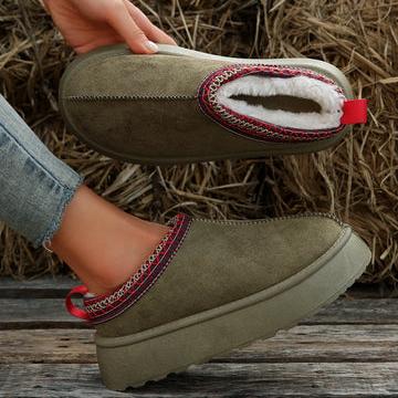 Scarpe invernali da donna in pelle scamosciata verde, con fodera in pelliccia sintetica bianca e dettagli rossi, su sfondo di paglia.