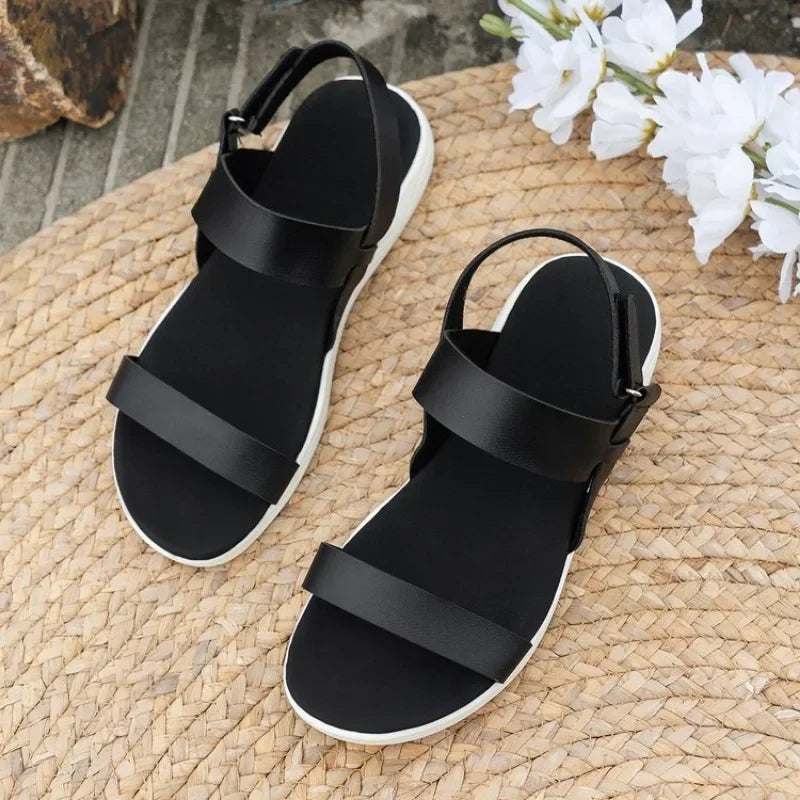 Sandali neri da donna su suola bianca, design minimalista, su tappeto intrecciato, fiori bianchi decorativi. Scarpe estive eleganti e comode.