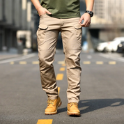 Uomo con pantaloni cargo beige e stivali gialli su strada urbana. Moda casual maschile, abbigliamento outdoor, stile urbano.