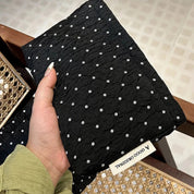 Mano che tiene una borsa trapuntata nera con motivo a pois bianchi, etichetta "A GOOD ORIGINAL". Accessorio moda elegante e moderno.