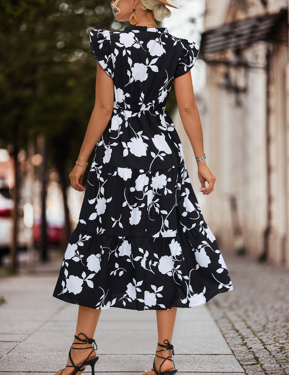 Abito lungo nero a fiori bianchi, donna di spalle, strada cittadina, sandali con tacco, look estivo elegante, moda femminile casual.