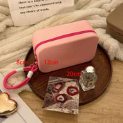 Astuccio rosa in silicone con cerniera rossa, dimensioni 20x12x8 cm, su vassoio di legno. Include profumo e accessori decorativi.