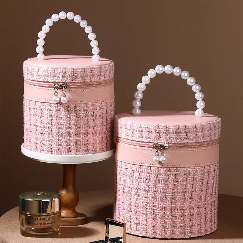Due eleganti borse cosmetiche rotonde rosa con manico di perle, tessuto intrecciato, su sfondo marrone. Ideali per trucco e accessori.