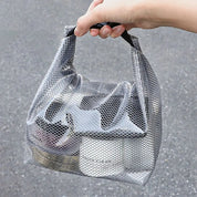 Borsa trasparente a rete con manico nero, contenente prodotti cosmetici. Design moderno, ideale per viaggi e organizzazione.