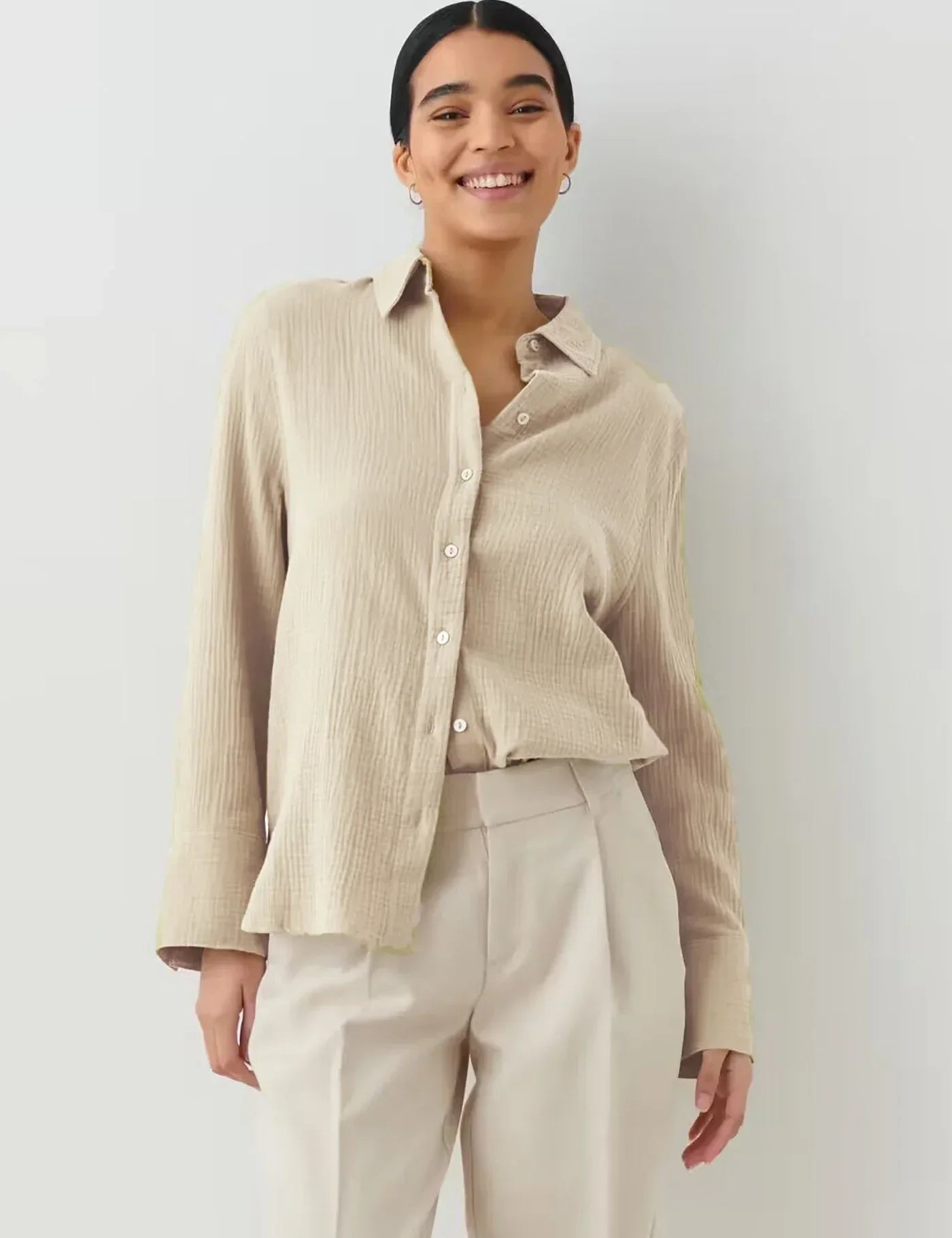 Donna sorridente con camicia beige a maniche lunghe e pantaloni chiari. Moda casual elegante, abbigliamento femminile, stile minimalista.