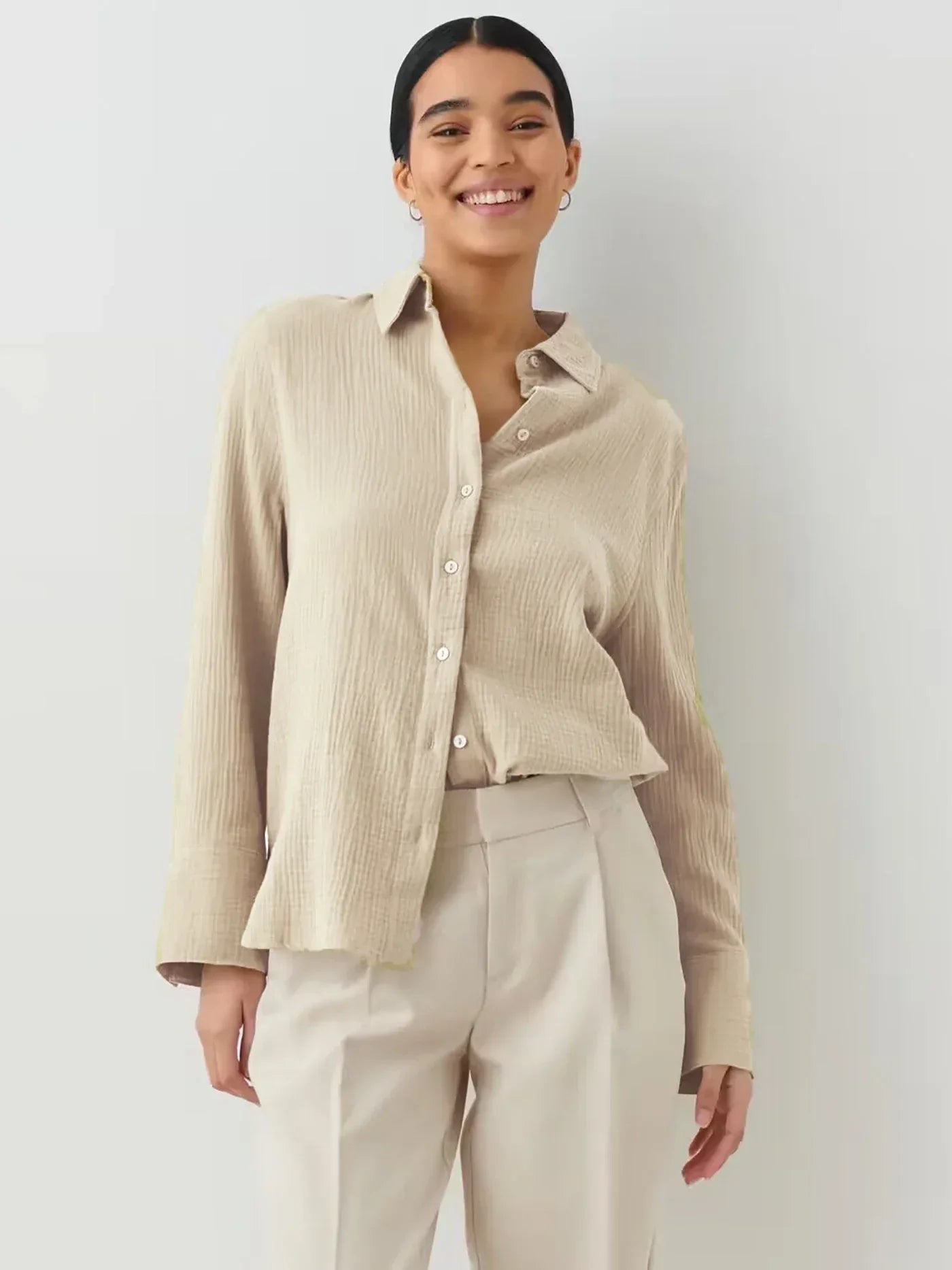 Donna sorridente con camicia beige a maniche lunghe e pantaloni chiari. Moda casual elegante, abbigliamento femminile, stile minimalista.