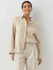 Donna sorridente con camicia beige a maniche lunghe e pantaloni chiari. Moda casual elegante, abbigliamento femminile, stile minimalista.