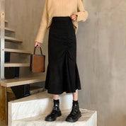 Gonna nera a vita alta con arricciatura, abbinata a maglione beige e stivaletti neri lucidi, moda autunno inverno, donna su scala moderna.
