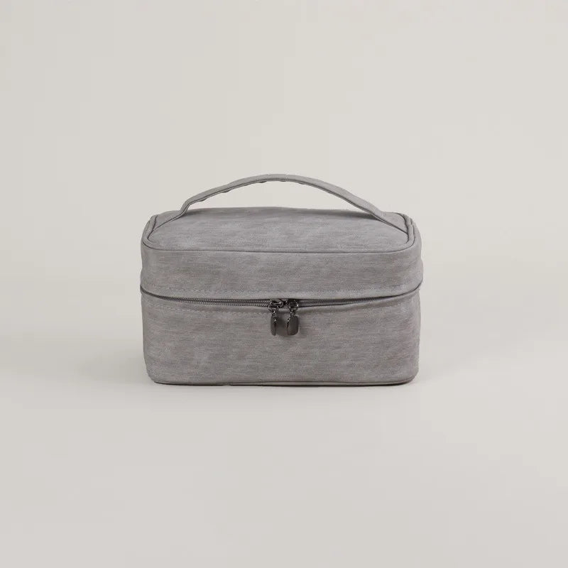 Borsa da viaggio grigia in tessuto, con manico superiore e chiusura a zip. Ideale per organizzare accessori e cosmetici. Design compatto e moderno.