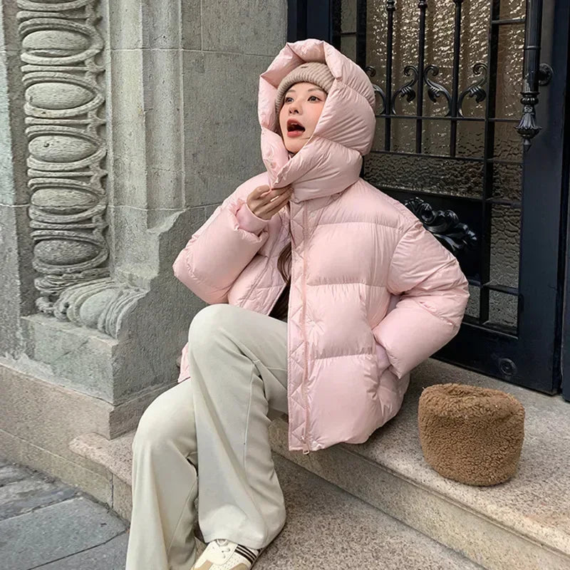 Giacca invernale rosa imbottita, donna seduta su gradino in città. Moda casual, cappuccio ampio, pantaloni chiari, stile urbano.