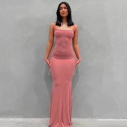 Abito lungo rosa aderente, senza maniche, indossato da una donna su sfondo grigio. Moda elegante, abbigliamento femminile, stile moderno.