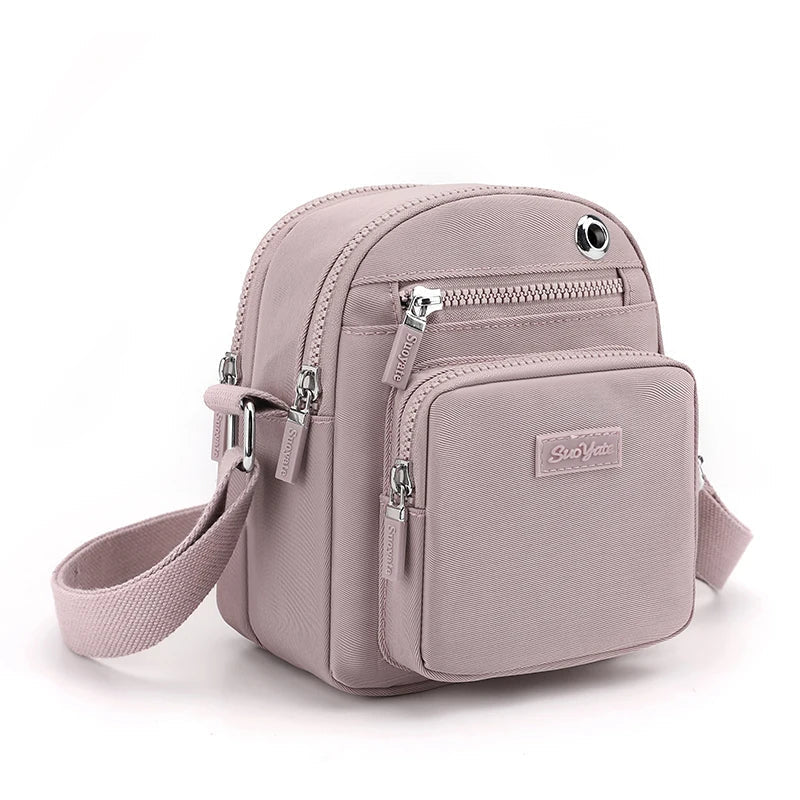Zaino compatto rosa chiaro in tessuto, con tasche multiple e cerniere argentate, ideale per moda donna, accessori viaggio, stile casual.