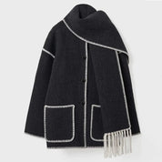 Cappotto nero in lana con bordi bianchi, tasche frontali e sciarpa integrata con frange. Elegante e caldo, ideale per l'inverno.