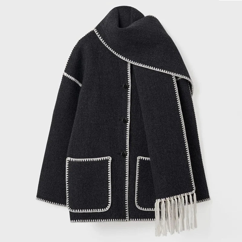 Cappotto nero in lana con bordi bianchi, tasche frontali e sciarpa integrata con frange. Elegante e caldo, ideale per l'inverno.