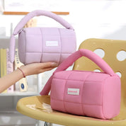 Due borse trapuntate in tessuto morbido, una rosa e una lilla, con manico imbottito, su sedia gialla. Design moderno, moda femminile, accessori eleganti.