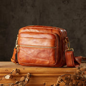 Borsa a tracolla in pelle marrone su tavolo di legno, design elegante e vintage, con cerniere dorate. Accessorio moda uomo/donna.