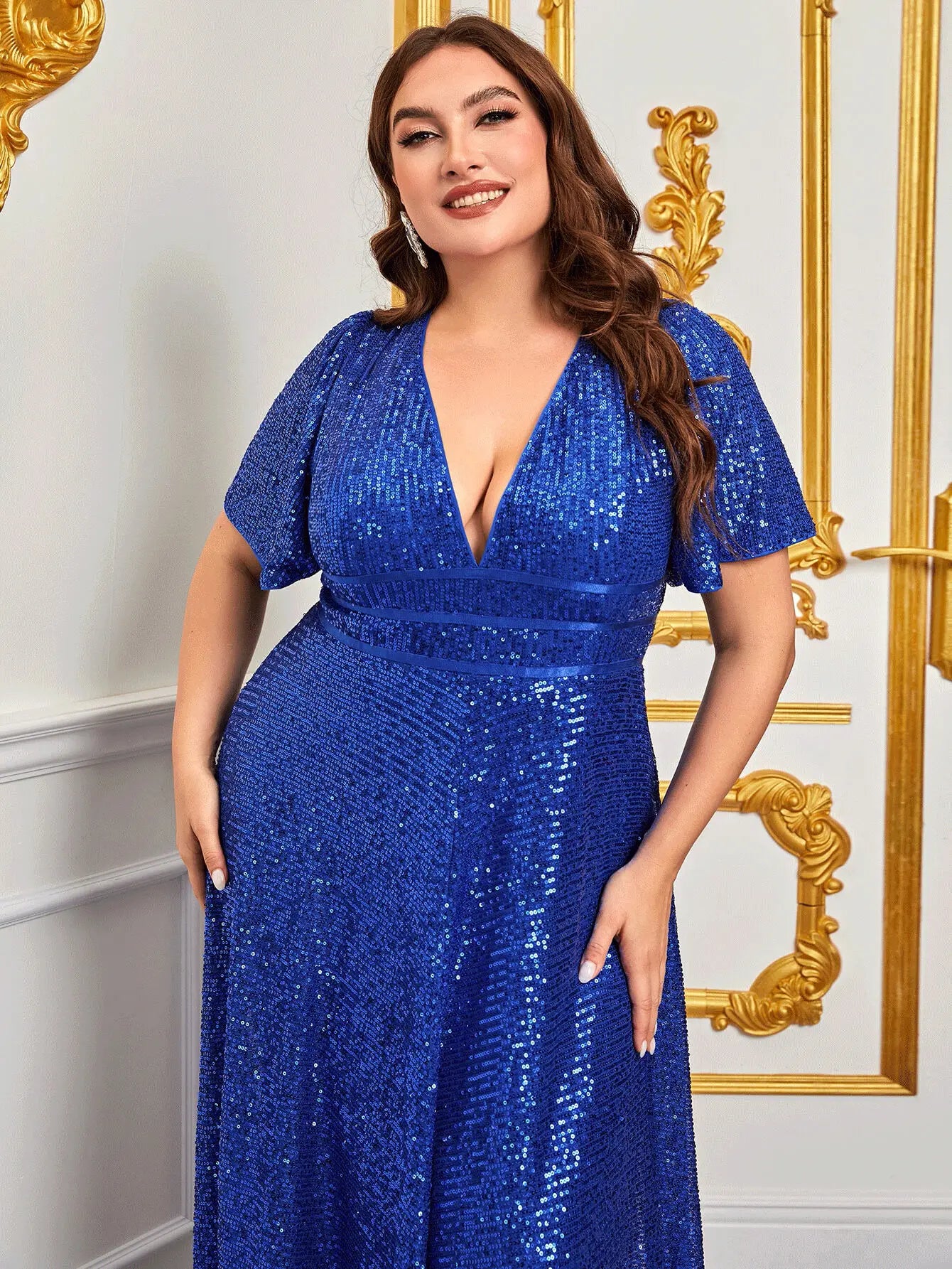 Abito lungo blu con paillettes, scollo a V profondo, maniche corte, indossato da una donna sorridente in un ambiente elegante con dettagli dorati.