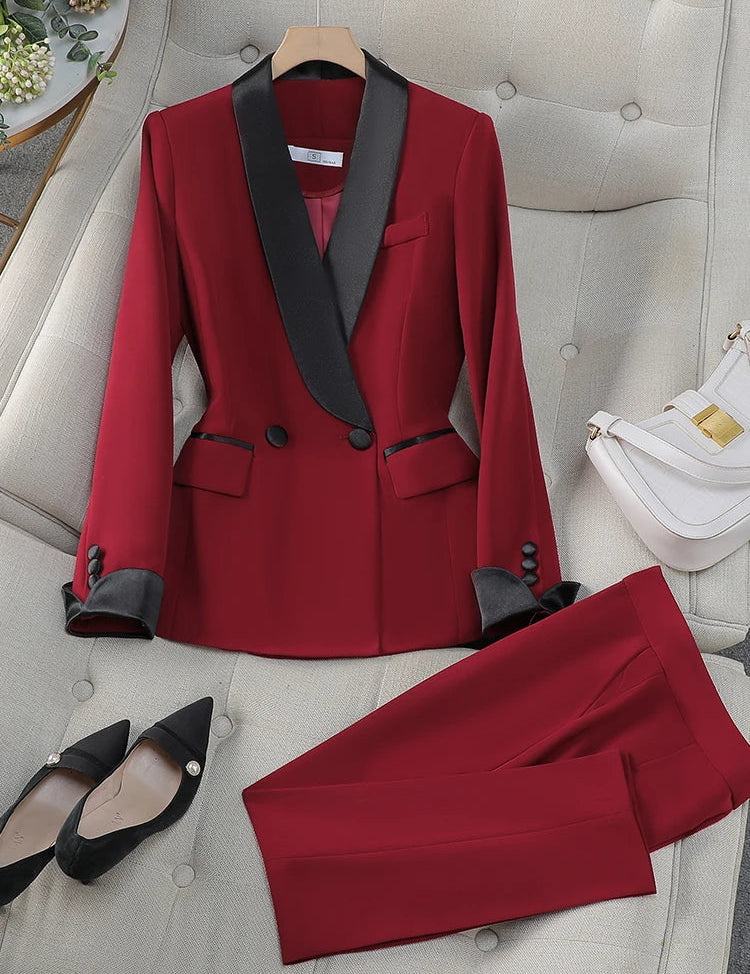 Completo da donna elegante rosso con giacca a doppio petto e pantaloni, dettagli neri, scarpe nere a punta, borsa bianca su divano beige.