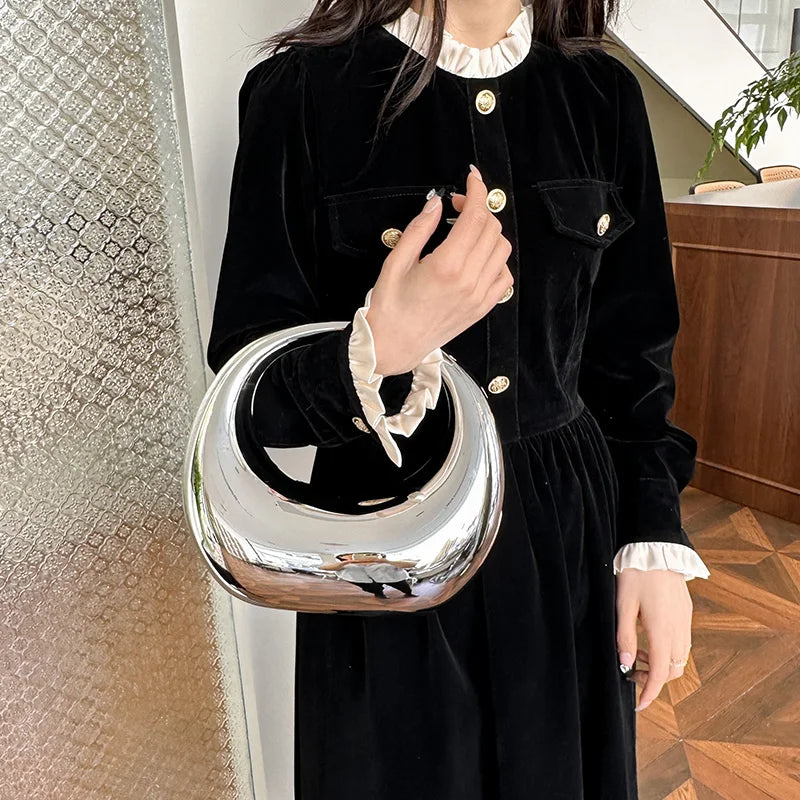 Donna con abito nero elegante e borsa a mano argentata lucida, design moderno. Moda femminile, accessori di lusso, stile contemporaneo.