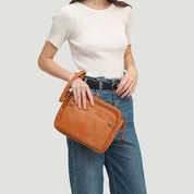 Donna con borsa a tracolla in pelle marrone, indossa maglietta bianca e jeans. Accessorio moda elegante, perfetto per look casual e quotidiani.