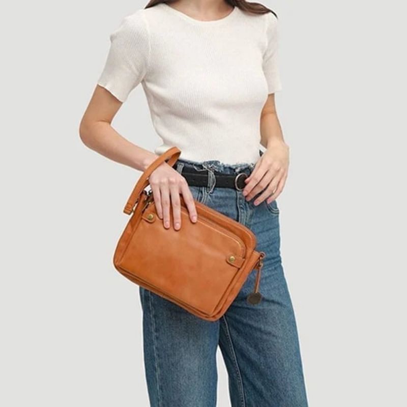 Donna con borsa a tracolla in pelle marrone, indossa maglietta bianca e jeans. Accessorio moda elegante, perfetto per look casual e quotidiani.