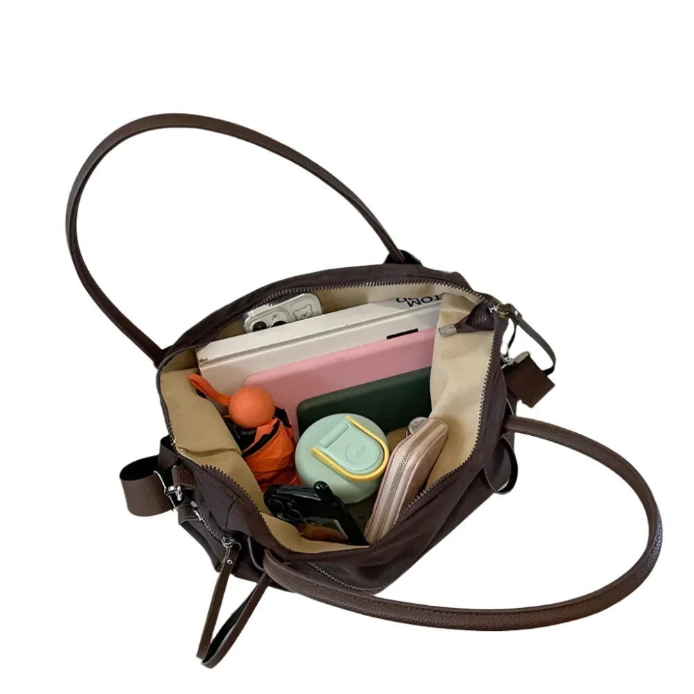 Borsa a tracolla marrone aperta, contenente accessori vari come portafoglio, occhiali, trucco e auricolari. Design elegante e spazioso.
