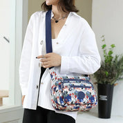 Donna con camicia bianca indossa borsa a tracolla floreale multicolore, design casual, moda femminile, accessorio pratico per tutti i giorni.