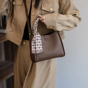Borsa a tracolla marrone in pelle con manico intrecciato, indossata da una persona in abito beige. Accessorio moda elegante e versatile.