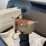 Borsa a tracolla piccola in pelle marrone e tessuto verde, con chiusura a bottone dorato, su divano nero. Accessorio moda elegante e versatile.