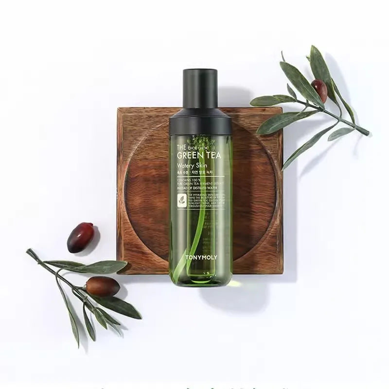 Bottiglia di tonico viso al tè verde TonyMoly su sfondo bianco, decorata con rami d'ulivo. Skincare coreana, idratante, naturale.