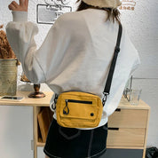 Donna con felpa bianca e borsa a tracolla gialla, in piedi davanti a un mobile in legno chiaro. Stile casual, moda urbana, accessori trendy.