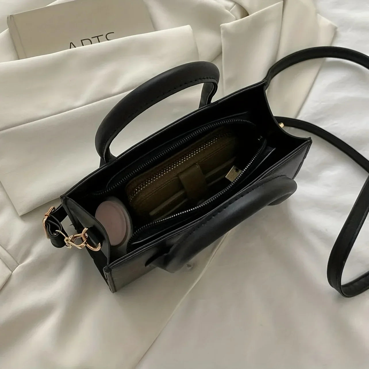 Borsa a tracolla nera in pelle, vista dall'alto, con cerniera dorata e manici, su sfondo bianco. Elegante accessorio moda donna.