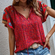Blusa rossa a fiori con maniche corte, scollo a V e dettagli floreali, indossata con jeans strappati. Moda estiva donna, stile casual chic.