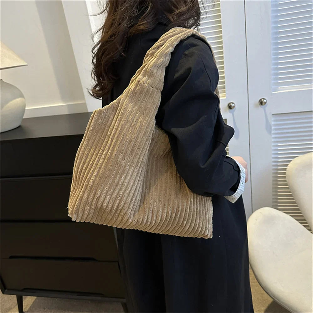 Donna con borsa a spalla in velluto a coste beige, abbigliamento casual nero, interni moderni. Accessori moda, stile autunnale, tendenze 2023.