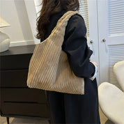 Donna con borsa a spalla in velluto a coste beige, abbigliamento casual nero, interni moderni. Accessori moda, stile autunnale, tendenze 2023.
