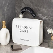 Borsa da toilette bianca con scritta "Personal Care", manico nero con perla, su ripiano bagno in marmo. Accessori trucco e cura personale.