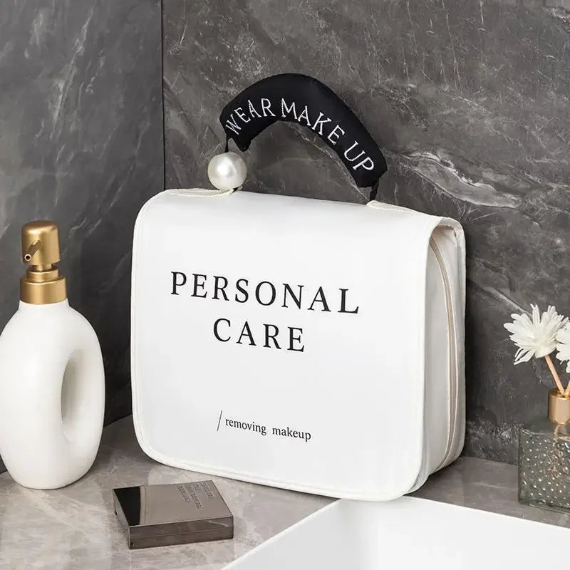 Borsa da toilette bianca con scritta "Personal Care", manico nero con perla, su ripiano bagno in marmo. Accessori trucco e cura personale.
