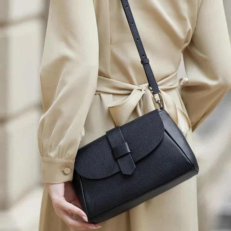 Borsa a tracolla nera in pelle, elegante e moderna, indossata su cappotto beige. Accessorio moda donna, perfetto per ogni occasione.