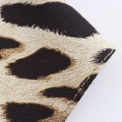 Stampa tessuto leopardato, motivo animalier su sfondo beige, dettaglio cucitura. Ideale per moda, abbigliamento, accessori.