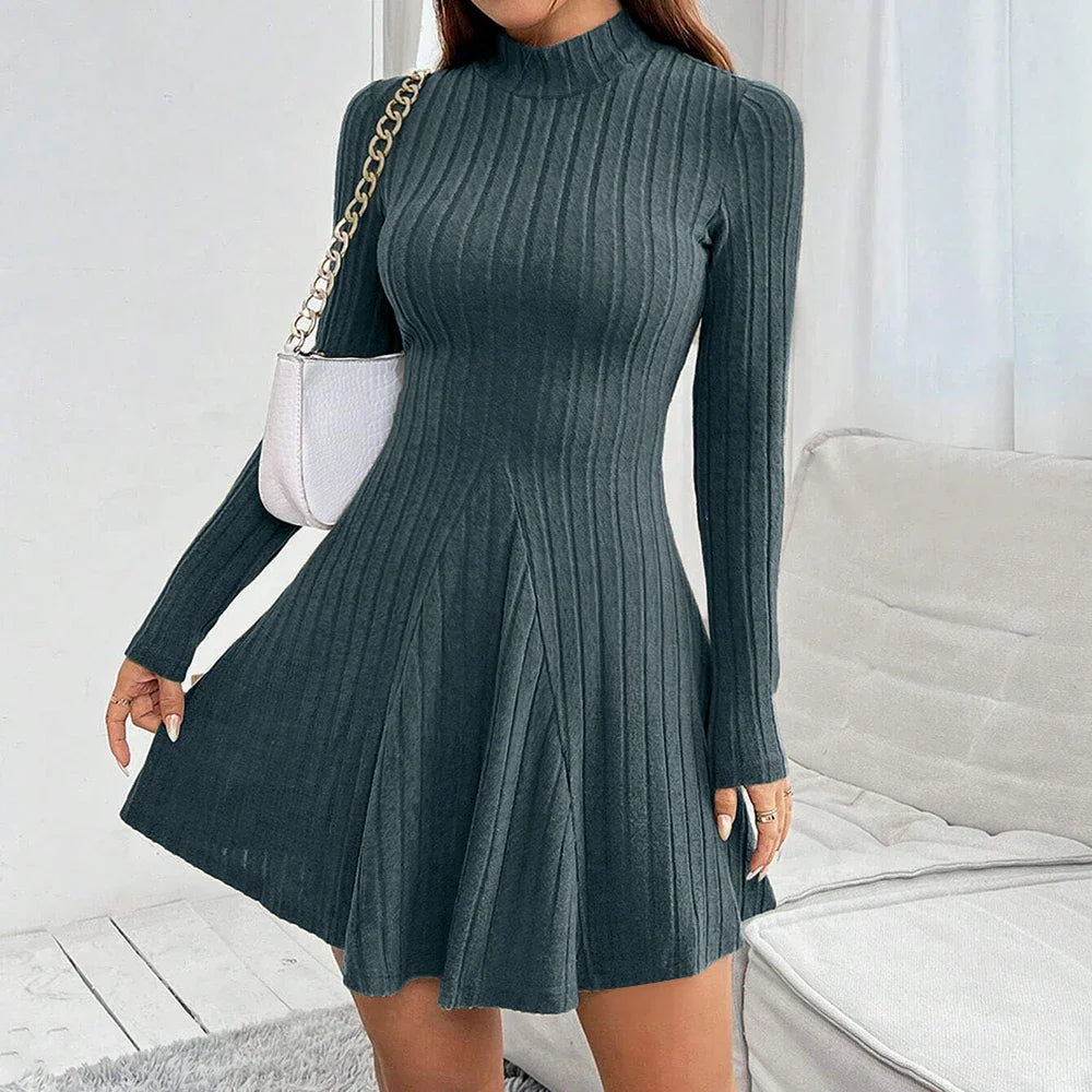 Vestito a maglia grigio scuro a coste, maniche lunghe, collo alto, abbinato a borsa bianca a tracolla. Elegante abbigliamento donna autunnale.