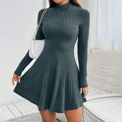 Vestito a maglia grigio scuro a coste, maniche lunghe, collo alto, abbinato a borsa bianca a tracolla. Elegante abbigliamento donna autunnale.