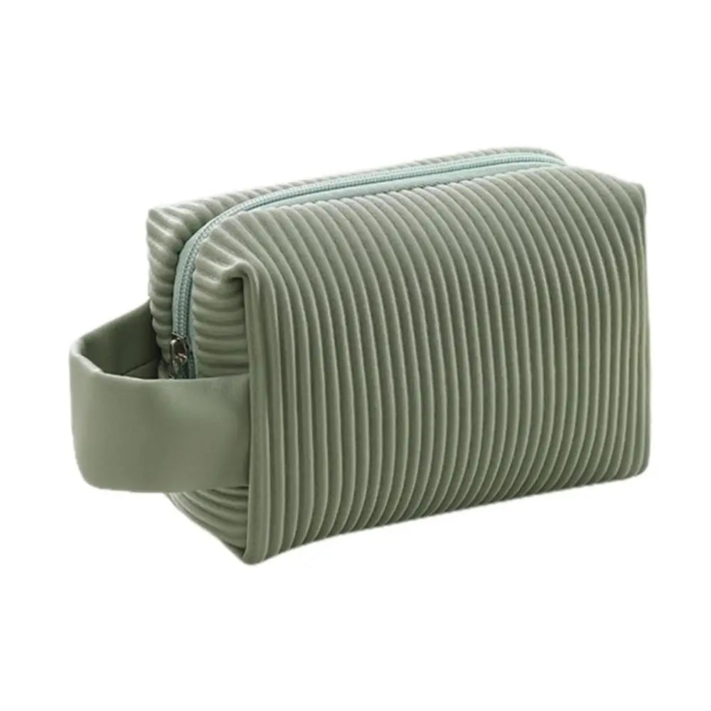 Astuccio da viaggio verde salvia con texture a coste, chiusura a zip e manico laterale. Ideale per cosmetici e accessori. Design moderno e funzionale.