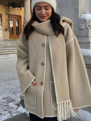 Donna con cappotto beige invernale con cappuccio e frange, davanti a edificio storico. Moda inverno, abbigliamento caldo, stile elegante.