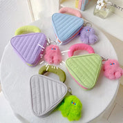 Cinque borse a forma di triangolo in colori pastello con portachiavi peluche colorati su un tavolo bianco. Design moderno e giocoso.