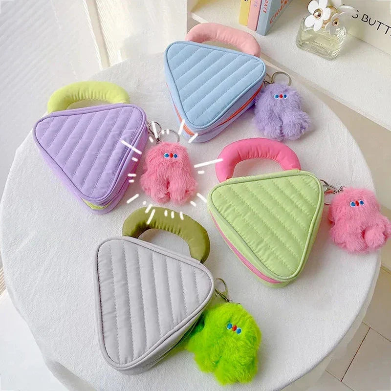Cinque borse a forma di triangolo in colori pastello con portachiavi peluche colorati su un tavolo bianco. Design moderno e giocoso.
