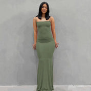 Abito lungo verde oliva aderente, senza maniche, indossato da una donna su sfondo grigio. Elegante e moderno, perfetto per eventi serali.